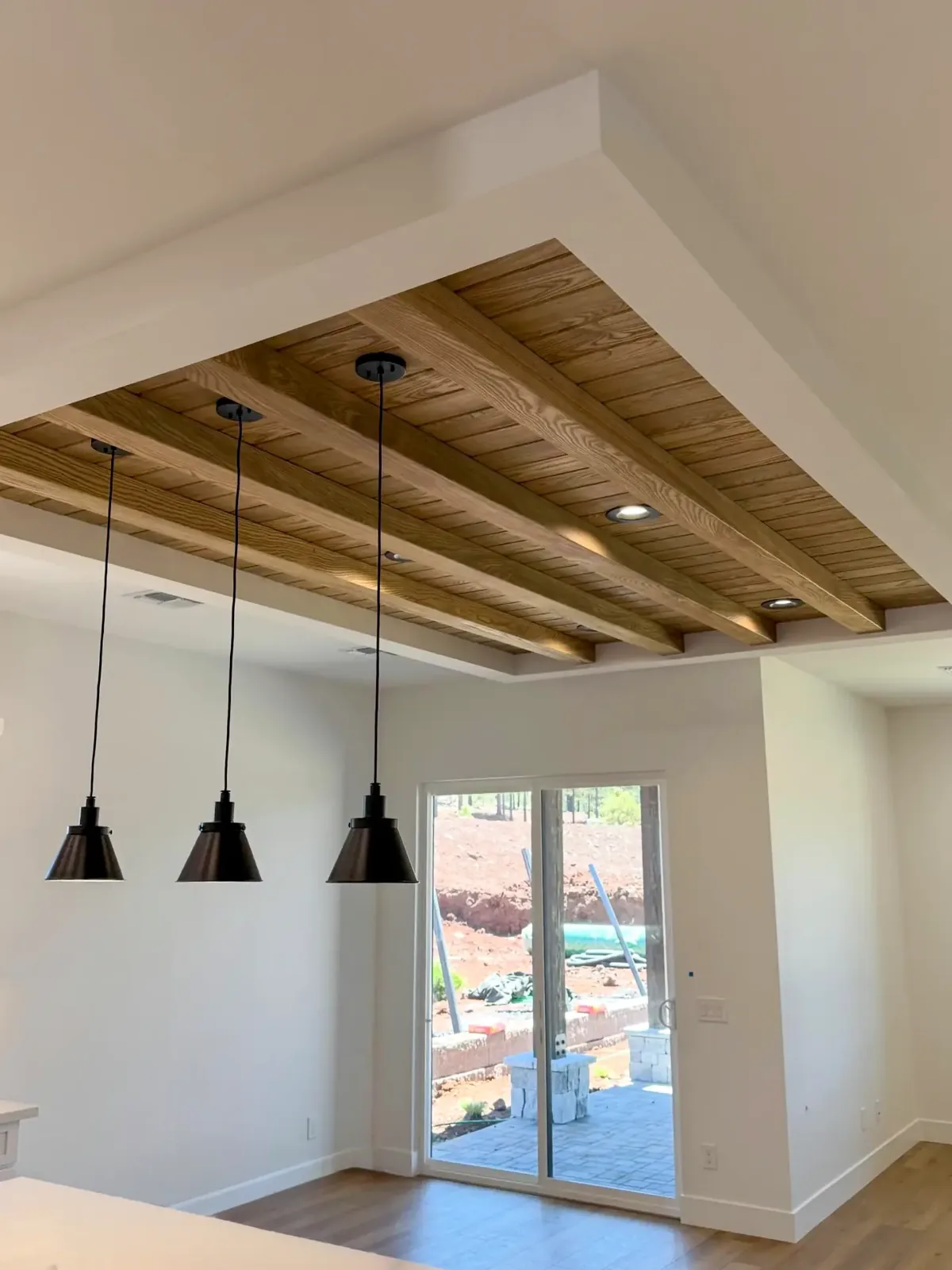 Recessed ceiling panel of wood beams with plank infill and recessed lights above three black pendant lights