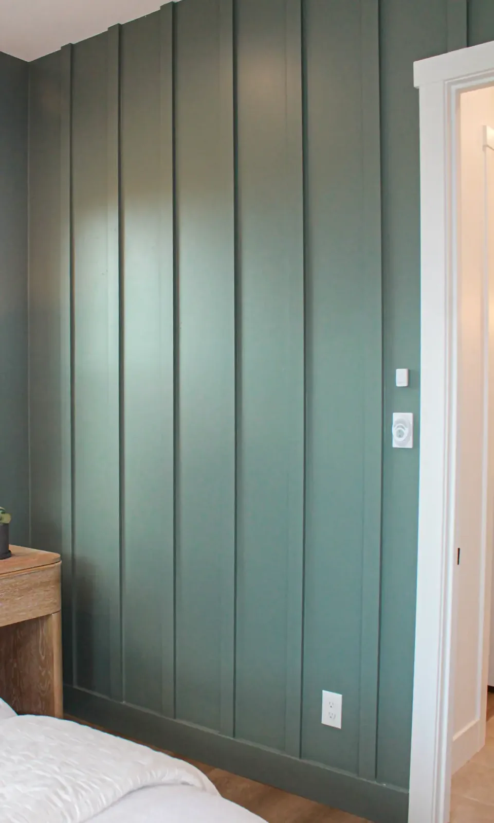 Green painted vertical board and batten bedroom wall with matching painted baseboard