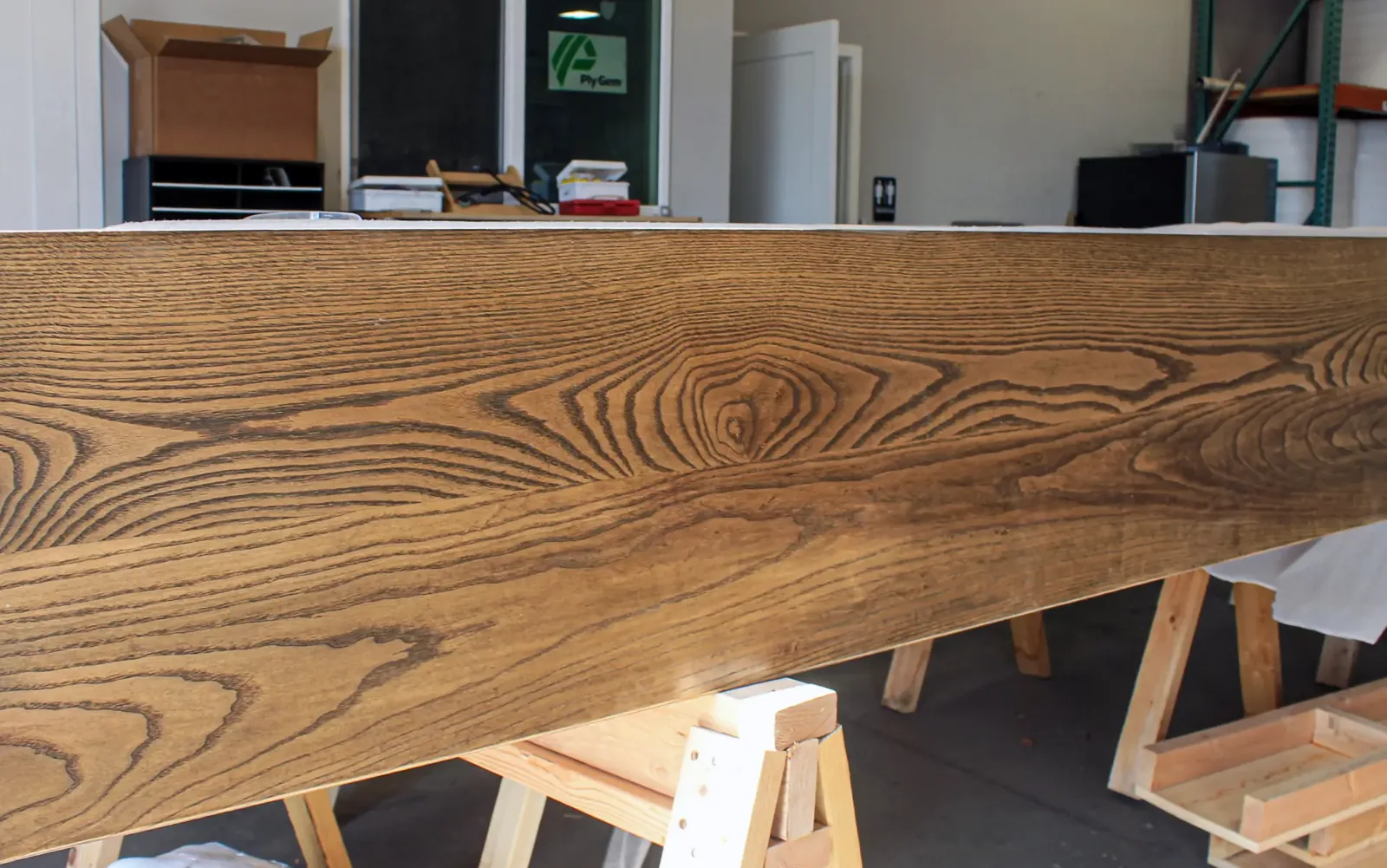 Long stained wood beam with heavy grain resting on sawhorses in the shop