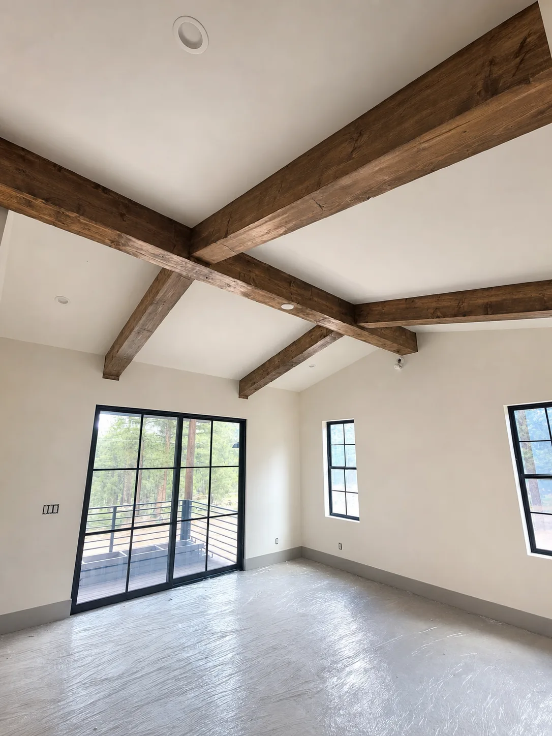 Room with exposed wood beams across a vaulted ceiling and black-framed windows