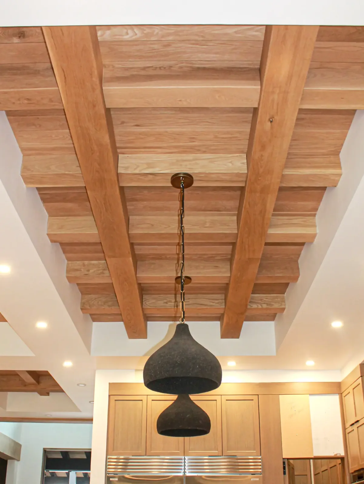 Recessed ceiling of wood beams with plank infill above a kitchen, with a pendant light hanging on a chain