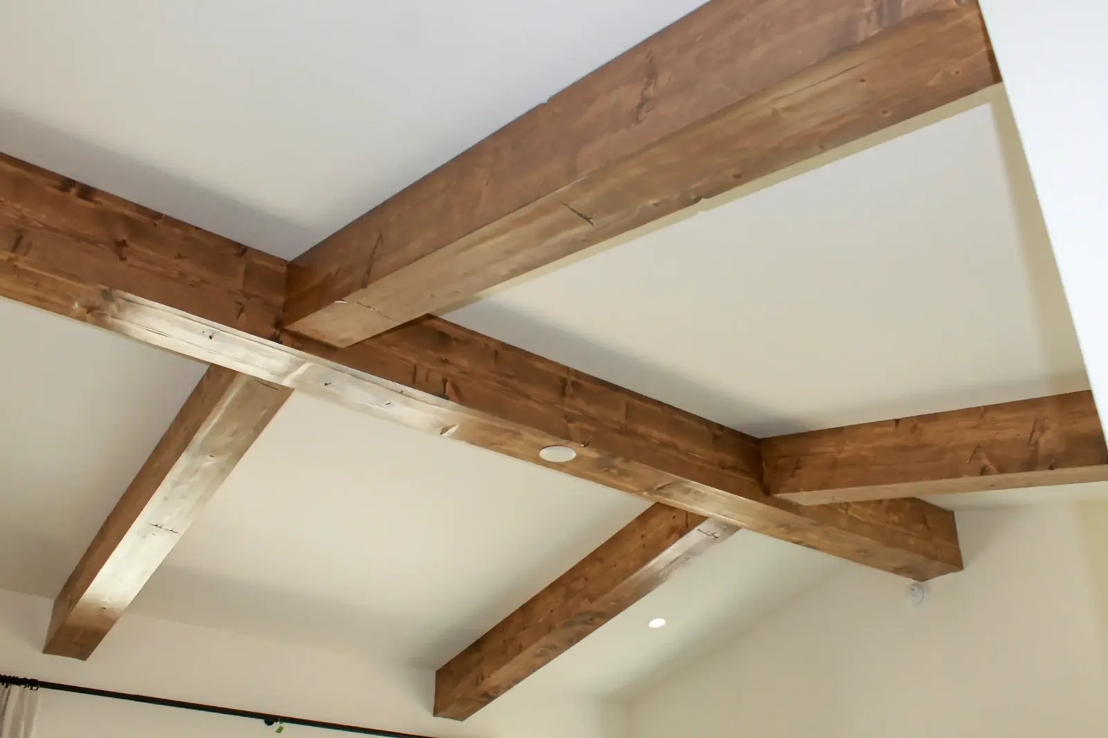 Stained wood beams in a grid across a white ceiling with a recessed light