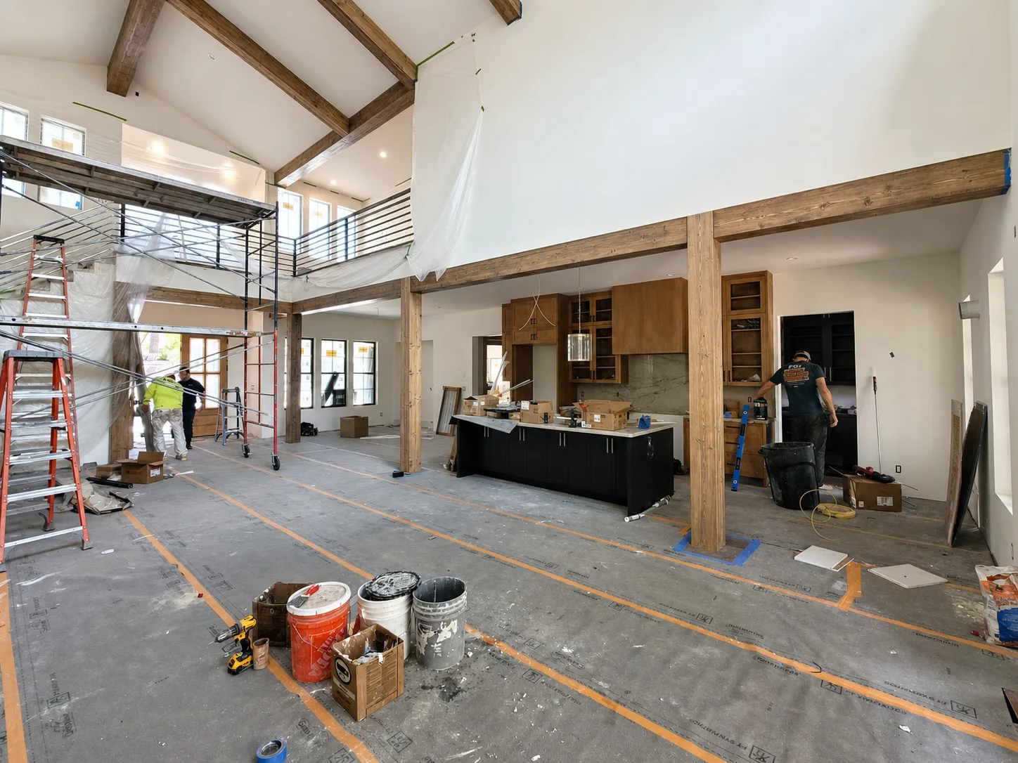 Great room during construction with exposed wood beams, timber posts, scaffolding, and protected flooring