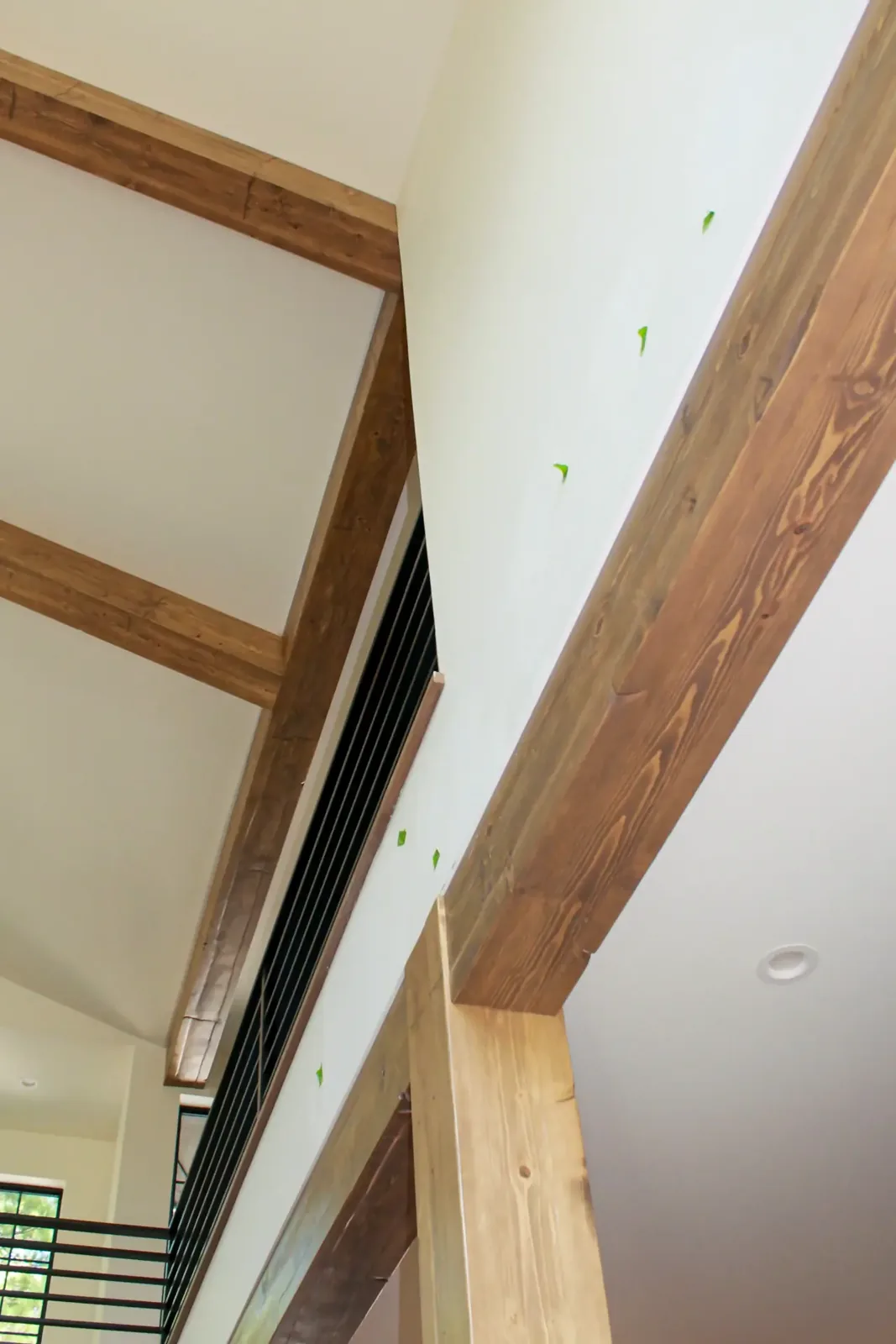 Stained ceiling beams and a wrapped wood column beside a two-story stair with a metal railing