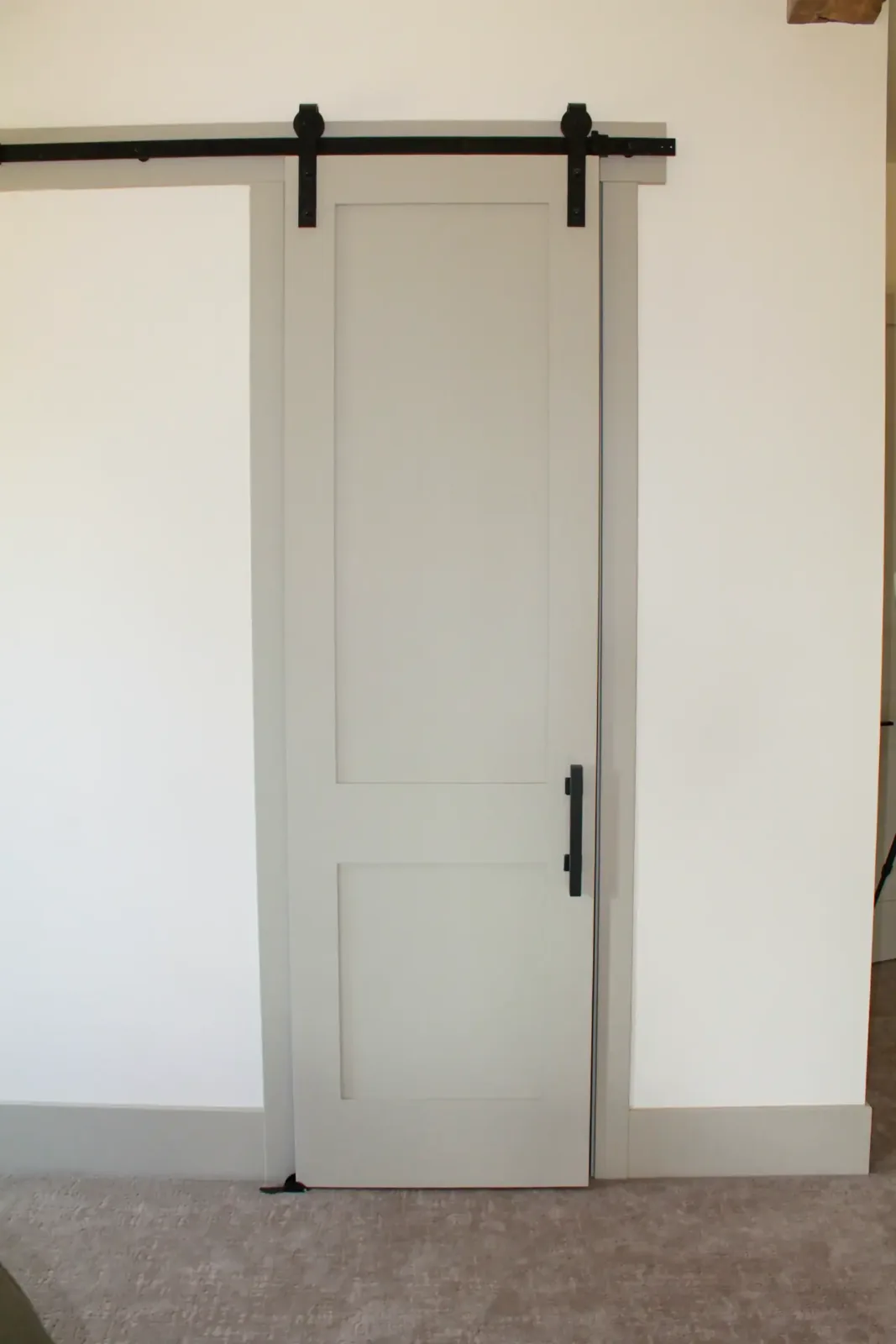 Painted two-panel sliding barn door on black track hardware with matching door casing