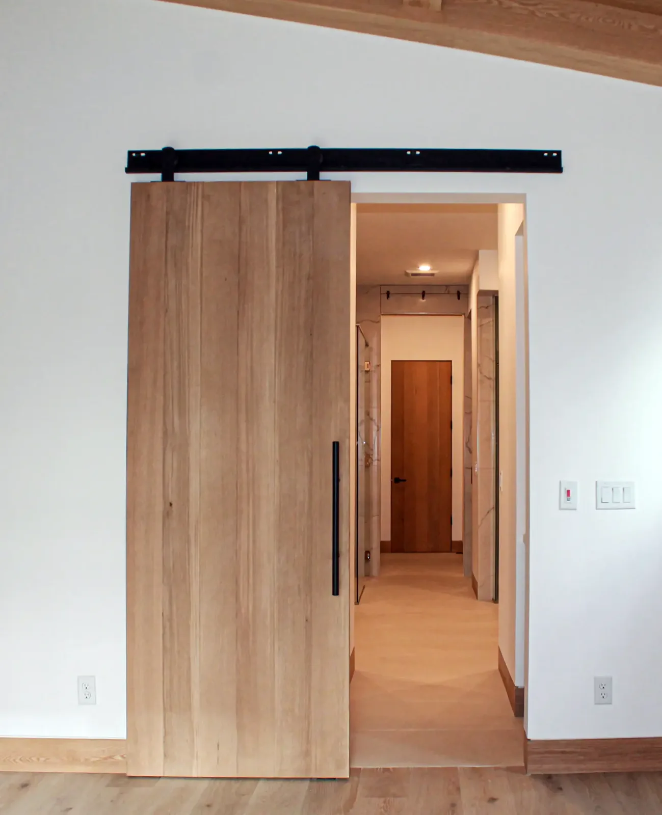 Wood slab sliding barn door on black track hardware, rolled open to a hallway