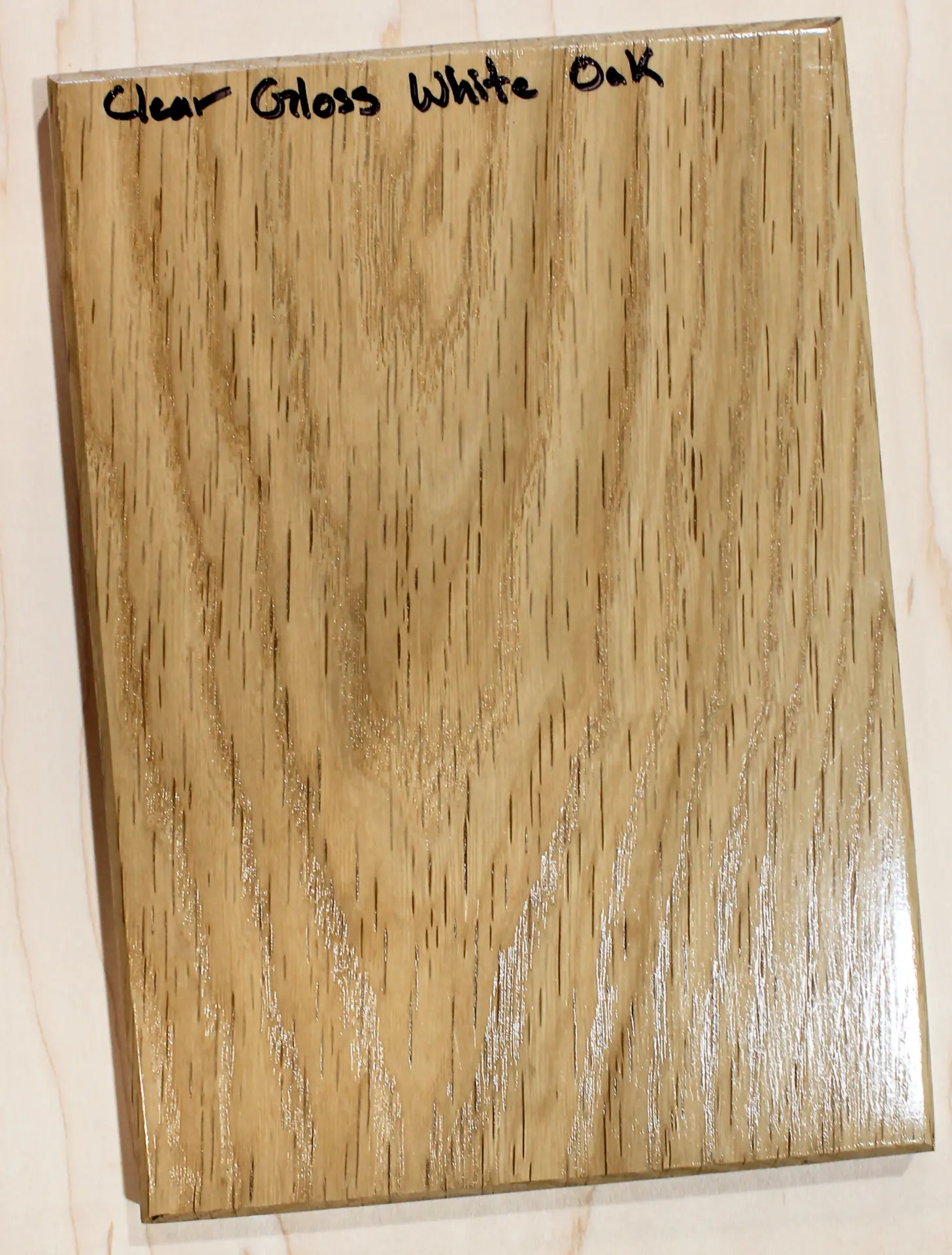 Finish sample board with a high-sheen clear topcoat over straight grain, hand labeled "Clear Gloss White Oak"