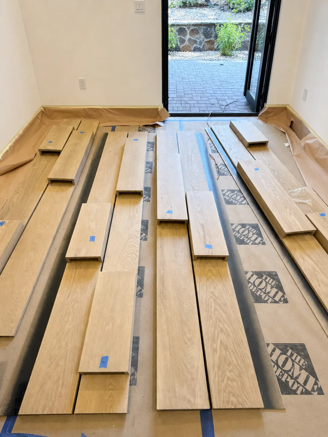 Milled wall panels laid out on floor protection before installation, labeled with blue tape