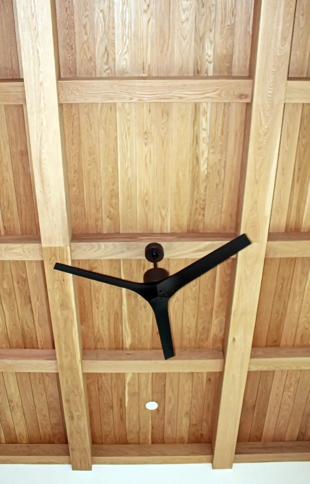 Wood plank ceiling framed by a grid of wood beams with a black three-blade ceiling fan