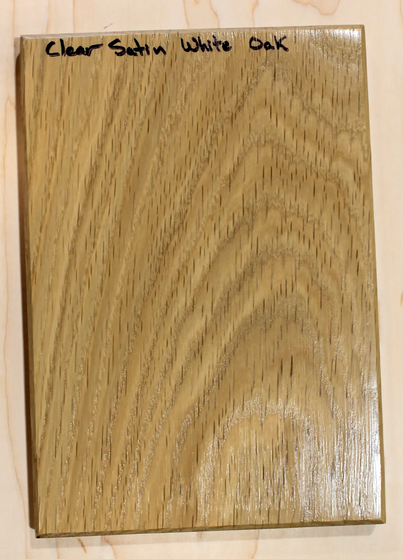 Finish sample board with a low-sheen clear topcoat over cathedral grain, hand labeled "Clear Satin White Oak"