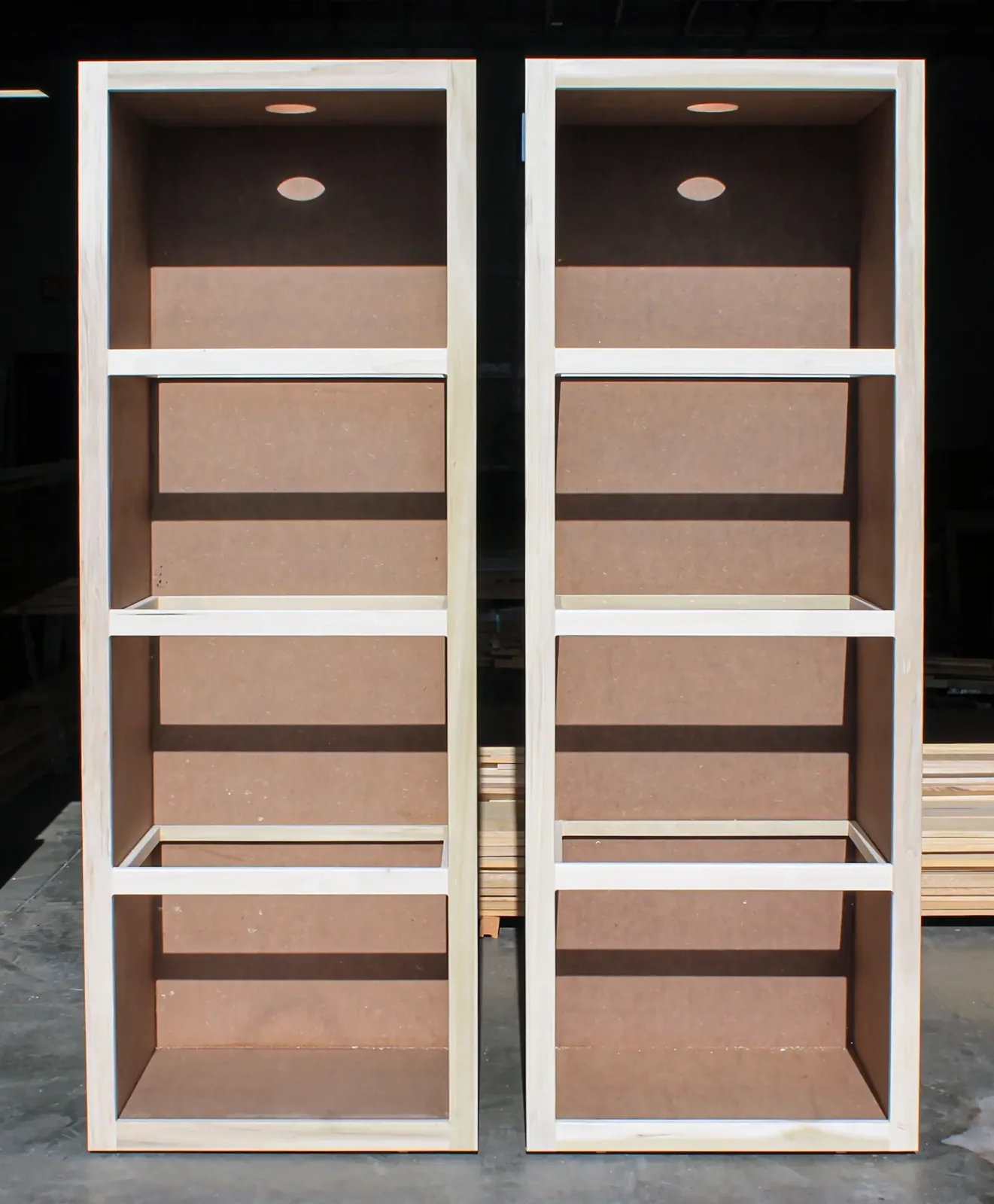Two tall unfinished shelving cabinet boxes standing side by side on a shop floor