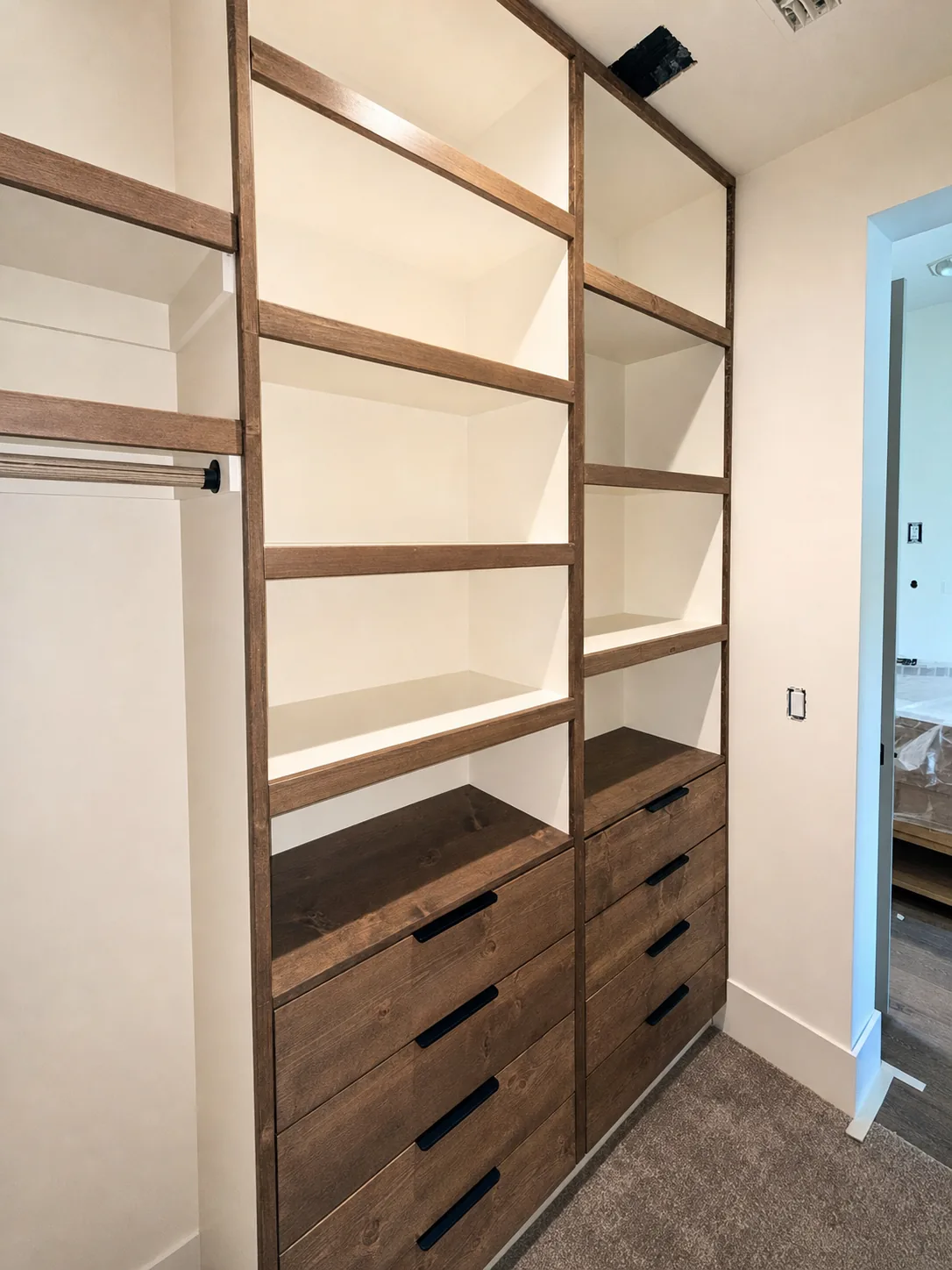 Closet built-in with tall open shelving, drawer banks, and adjacent hanging space